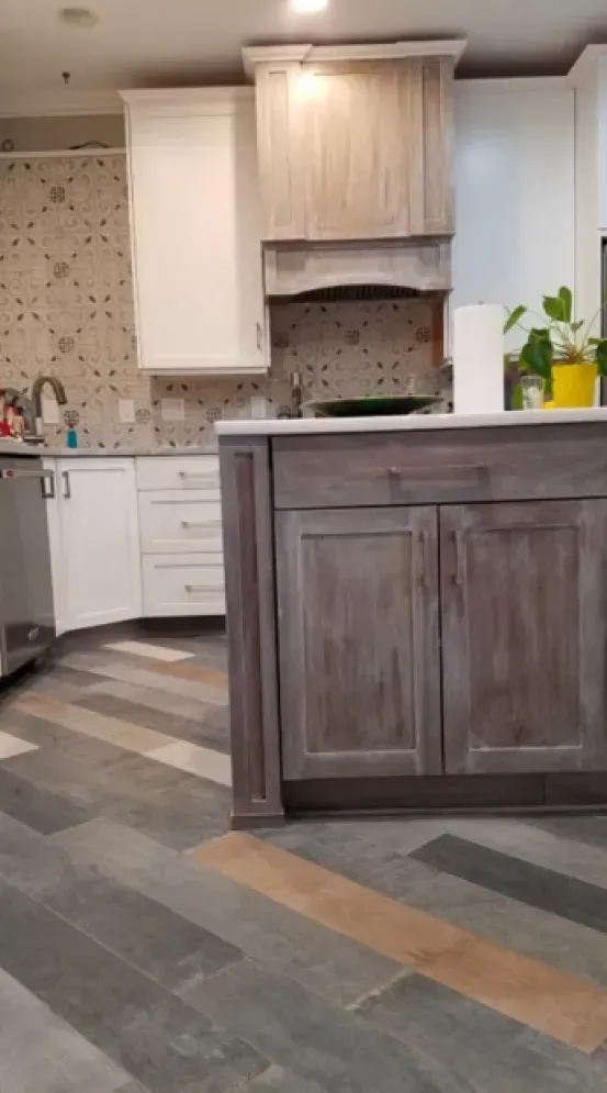 Modern kitchen with white cabinets, dark island, patterned backsplash, and gray wood-look flooring