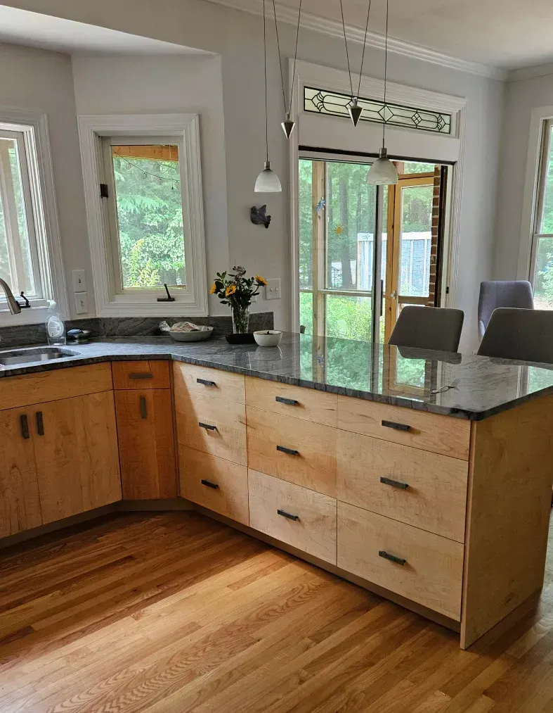 Bright kitchen with wood floors, granite island, and sliding glass doors to a deck.
