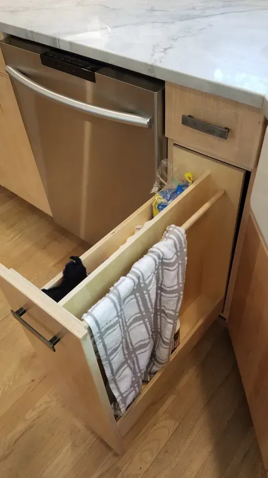 Open kitchen drawer with a pullout trash/recycling bin beside a stainless steel dishwasher