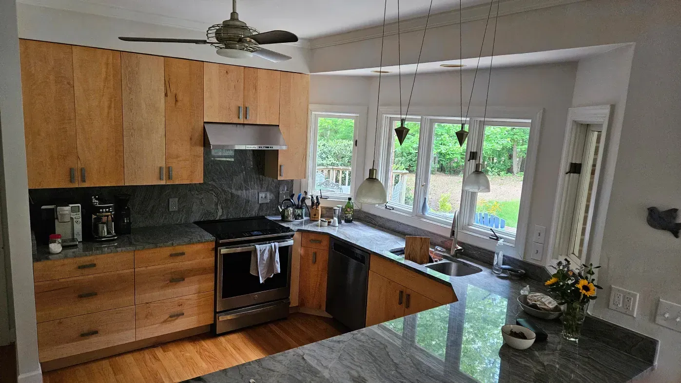 Modern kitchen with wood cabinets, black appliances, granite island, and bright windows over the sink.