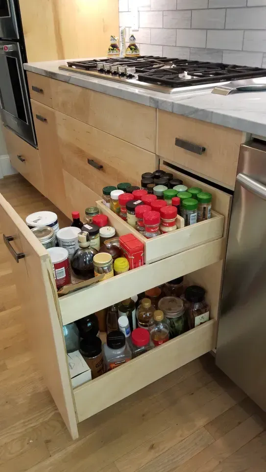 Kitchen pull-out drawers full of spices and condiments beside a stove and oven