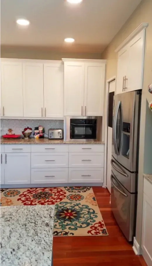 Modern white kitchen with stainless fridge, built-in oven, red rug, and patterned runner on wood floor