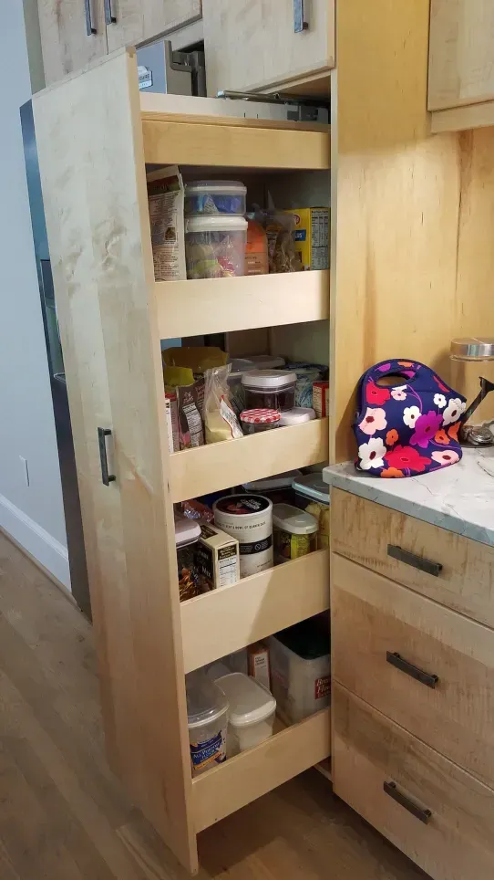 Open pantry cabinet with shelves of canned goods beside a kitchen counter and drawers.