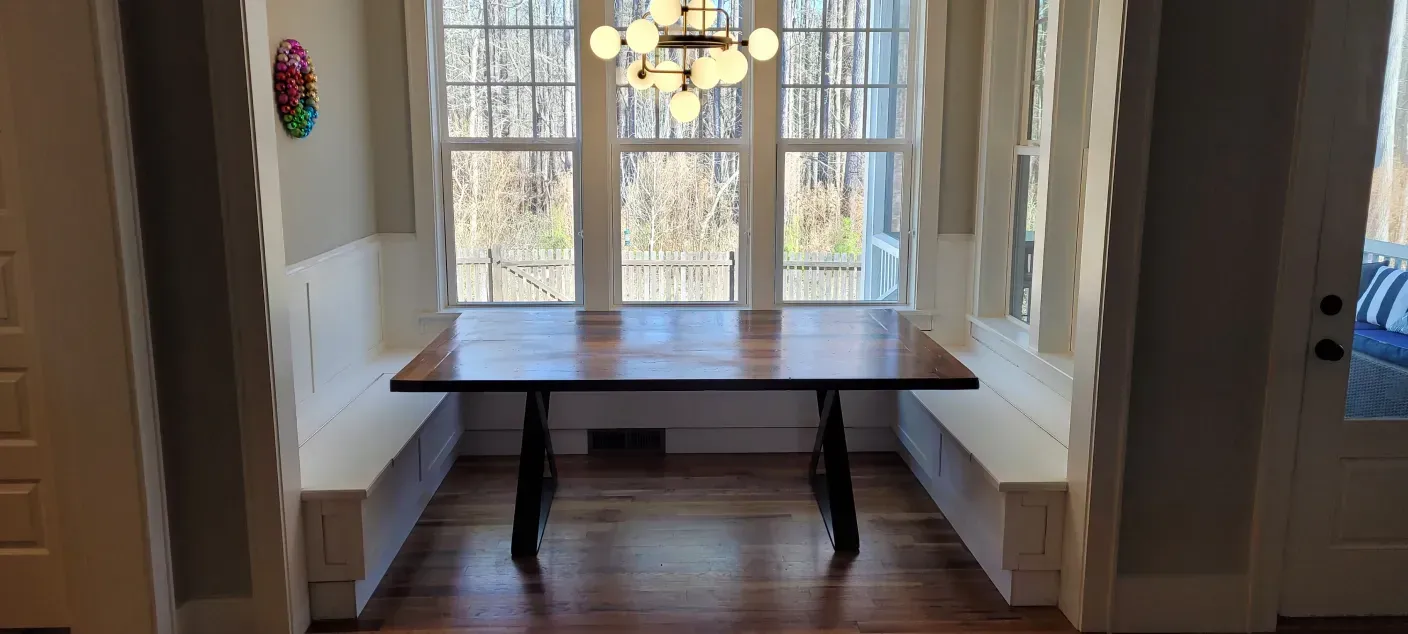 Dining table in a bright nook by windows, with built-in bench seating and hardwood floors