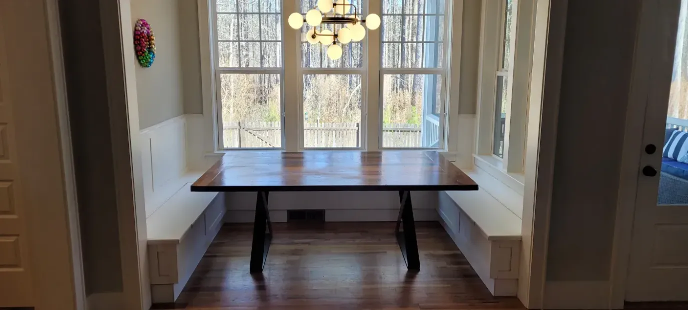 Dining nook with a dark wooden table centered between built-in bench seats in front of a bright window.