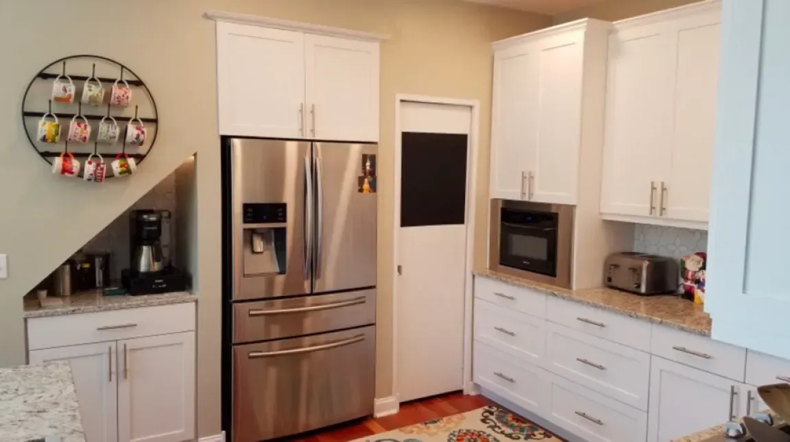 Modern kitchen with stainless steel fridge, white cabinets, microwave, and decorative wall shelves