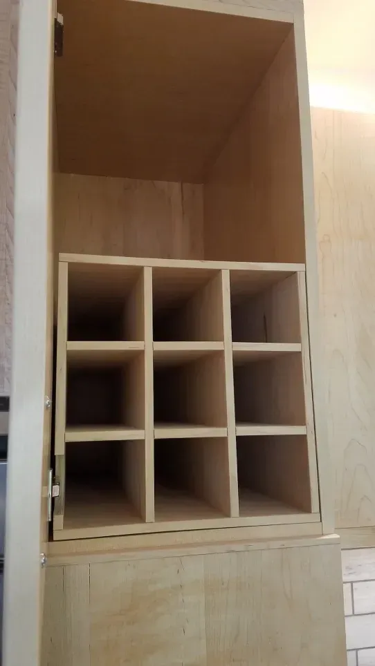 Wooden cabinet with open cubbies and a large empty top shelf against a light wall.