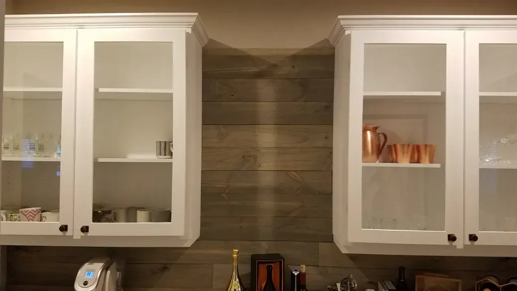 Kitchen cabinets with white shelves and glass doors flanking a wood plank backsplash.