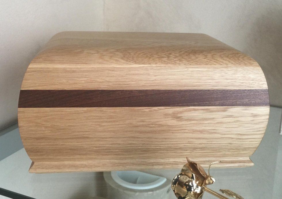 Scatola di legno con parte superiore curva e fascia marrone scuro.