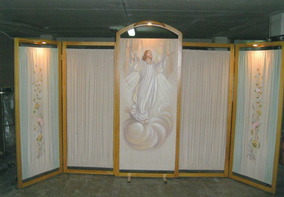 Una scena di angelo dipinta su uno sfondo con pannelli laterali e illuminazione, in una stanza buia.