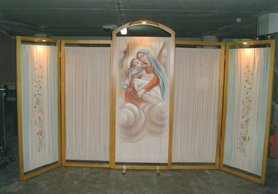 Un dipinto raffigurante la Vergine Maria e il bambino è esposto su un paravento pieghevole con luci attaccate.