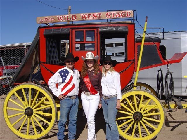 Three people standing in front of a stagecoach that says wild west stage
