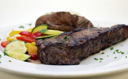 A white plate topped with a steak and vegetables