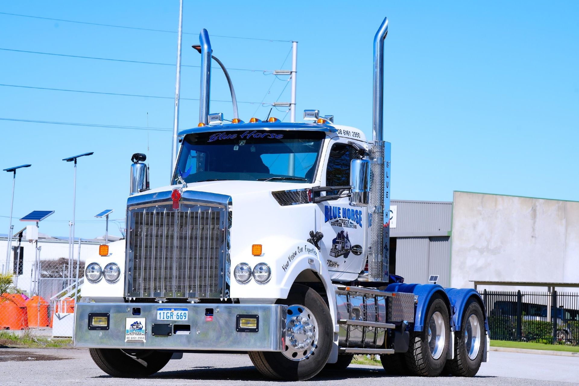 White and blue semi-truck with a silver grill, parked on a sunny day.