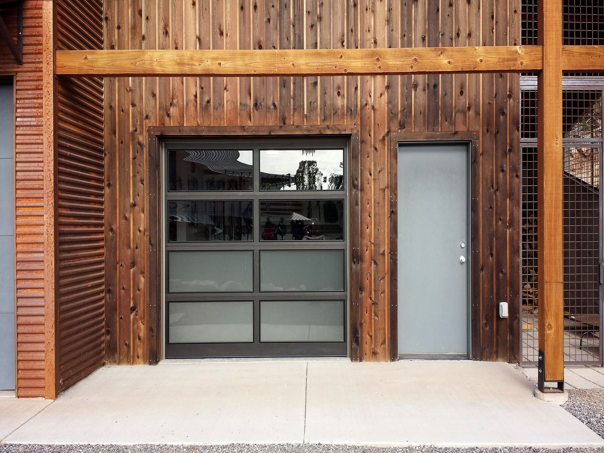 Modern building exterior featuring a wood-paneled wall, a gray pedestrian door, and a multi-panel glass garage door.