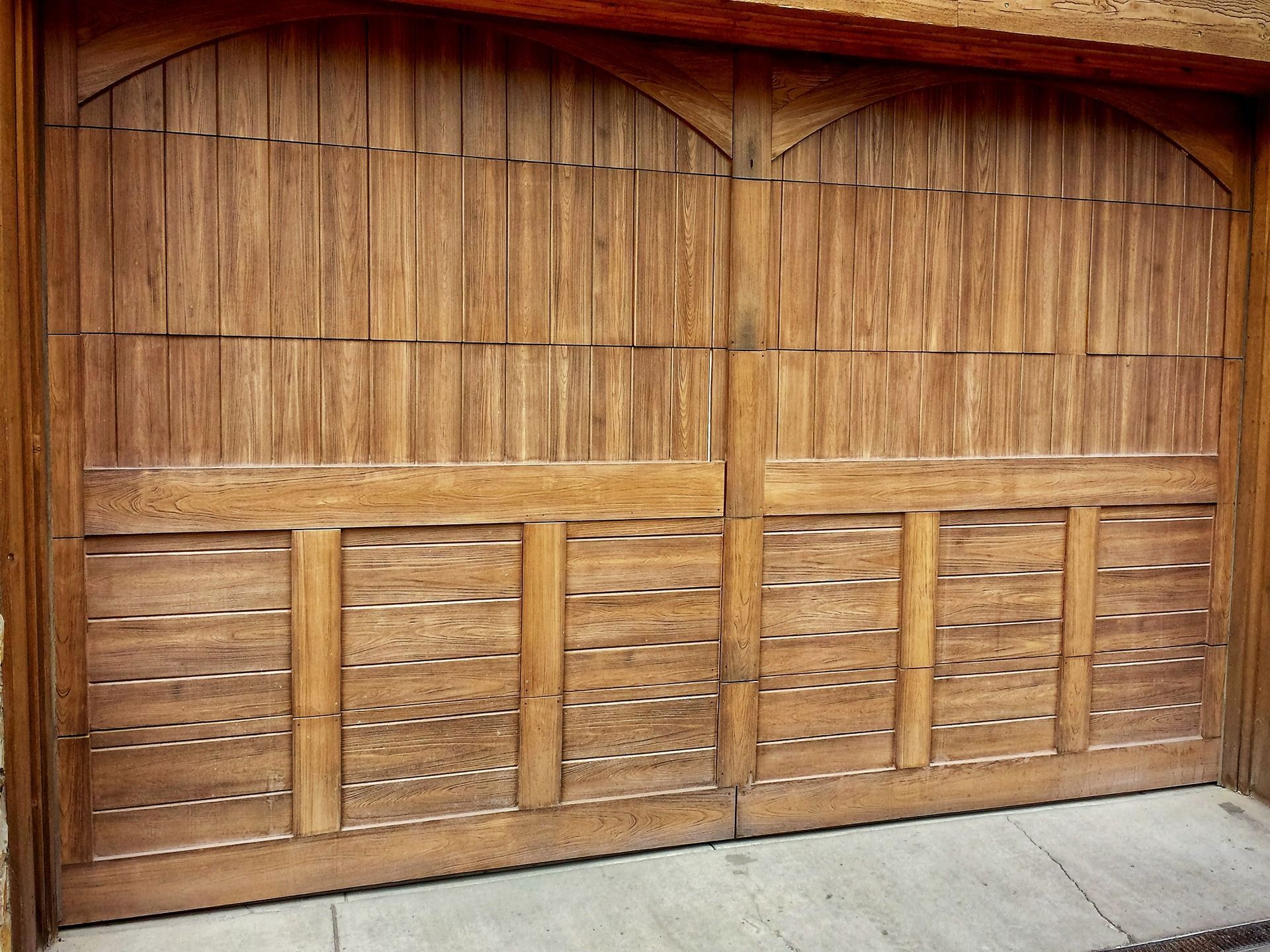 A rustic, two-panel wooden garage door with an arched top and decorative horizontal wood slats.