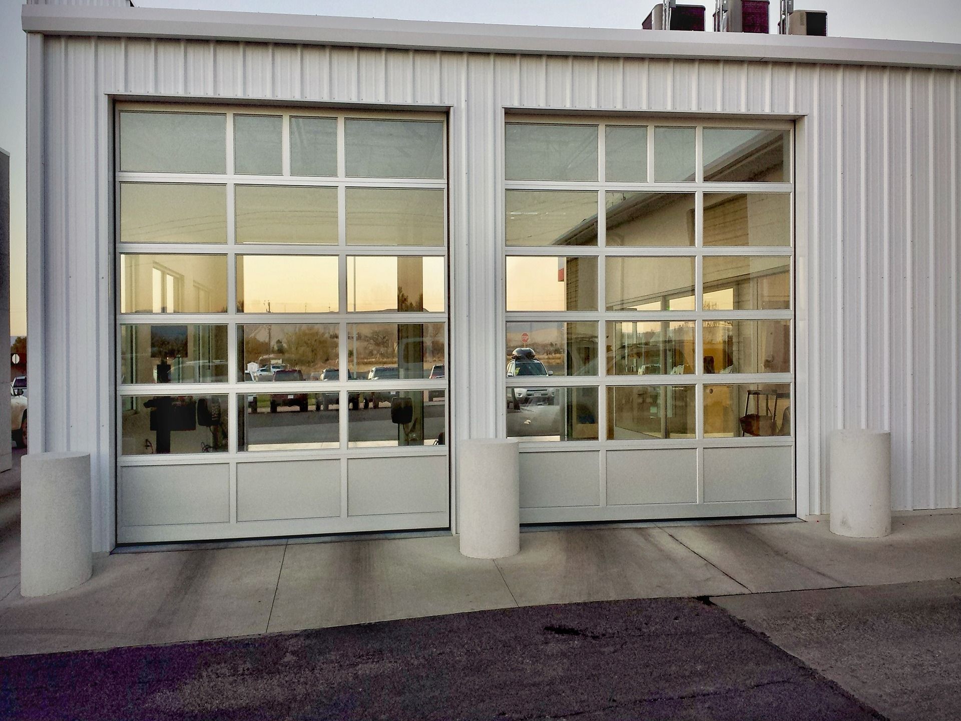 Two glass-paneled garage doors on a white building exterior with three concrete bollards in front.