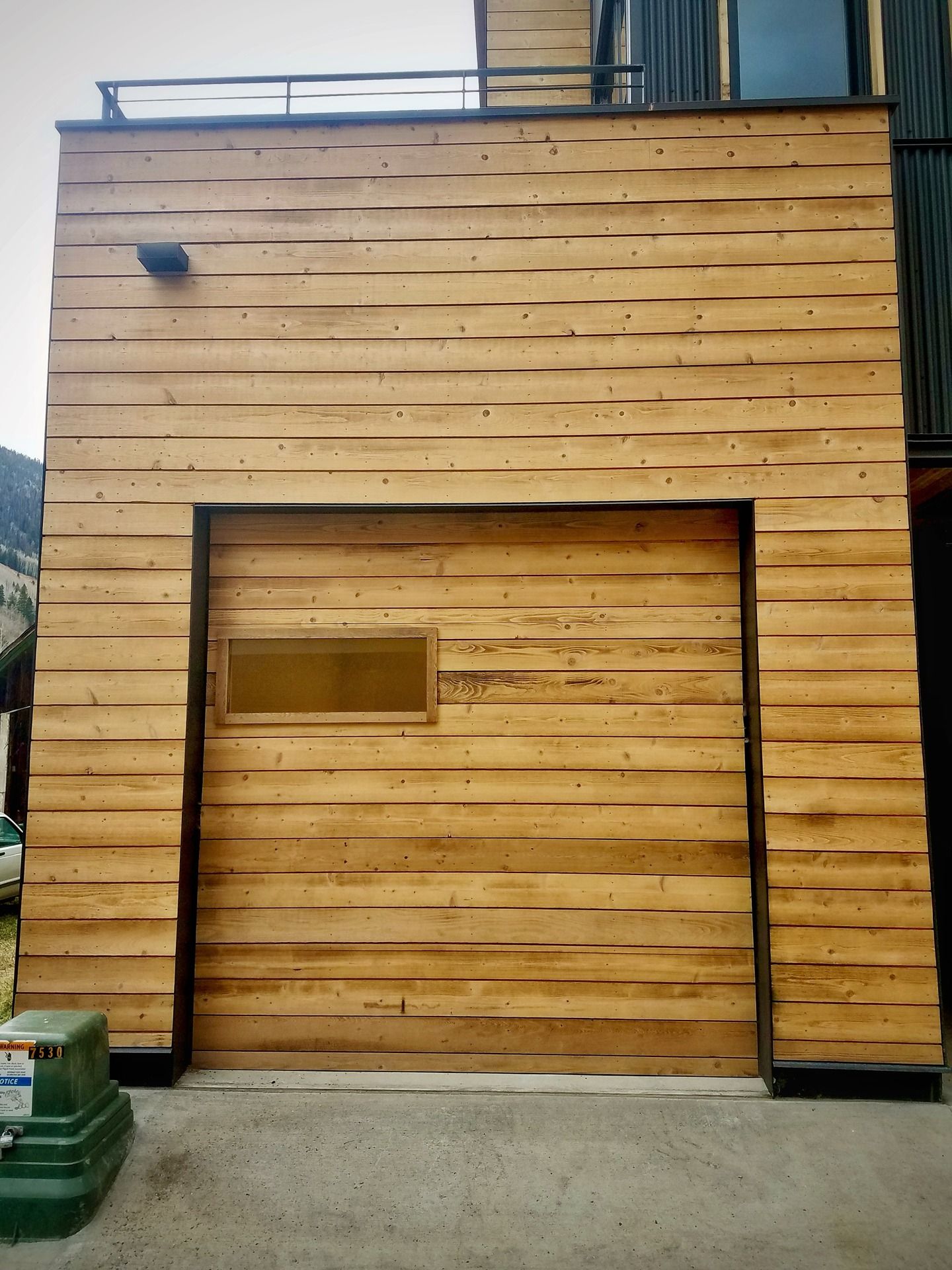 Garage door and surrounding exterior wall covered in light-colored, rustic horizontal wooden planks with a small window.