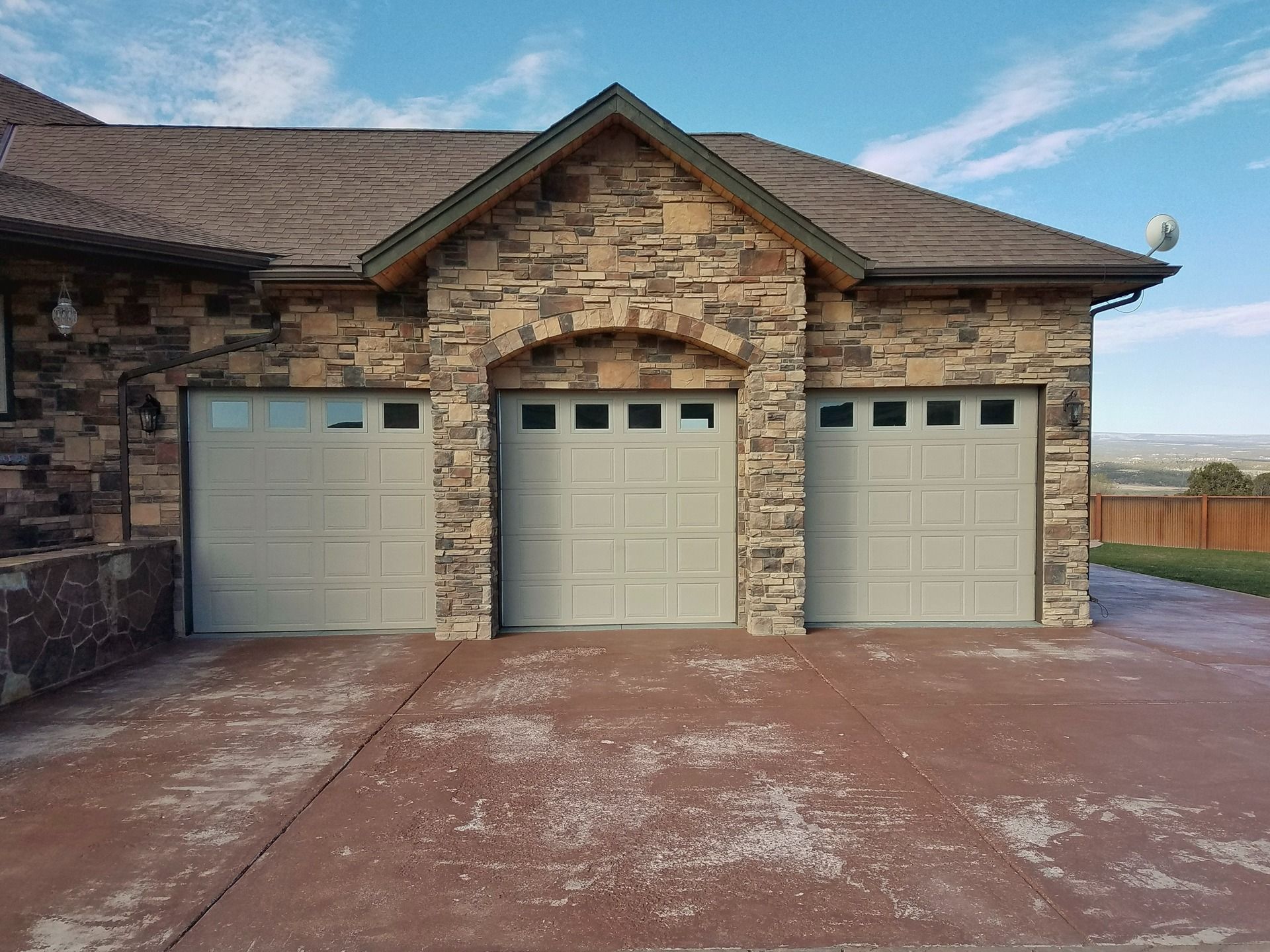 A three-car garage with light-colored doors set in a stone facade under a clear blue sky.