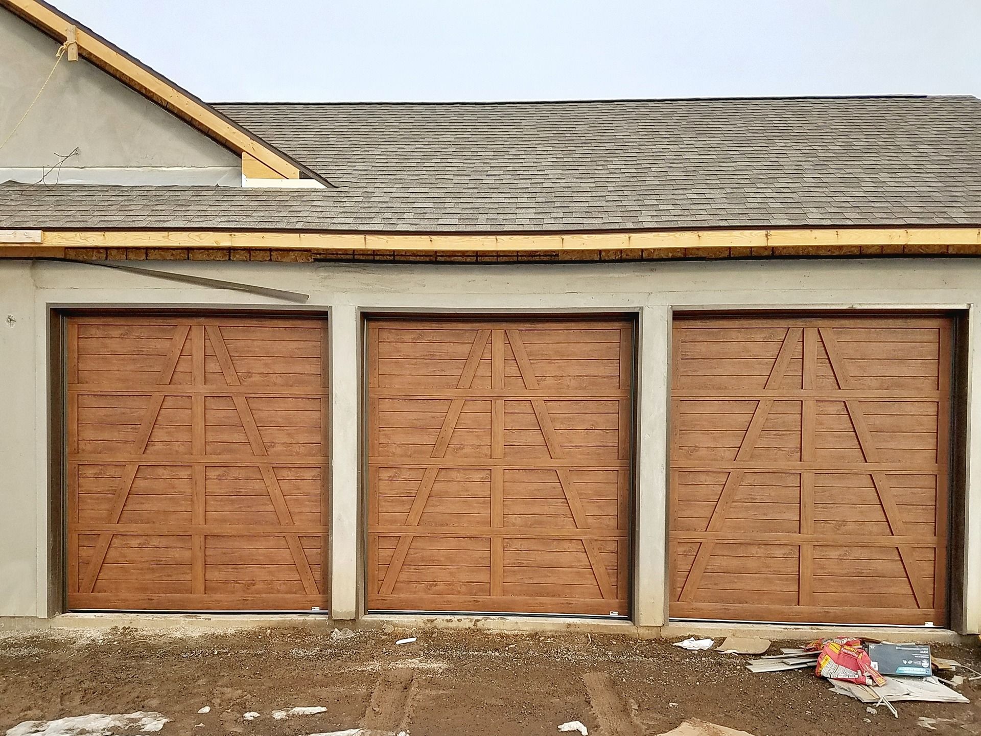 Three wooden, carriage-style garage doors with diagonal paneling on a modern home under construction.