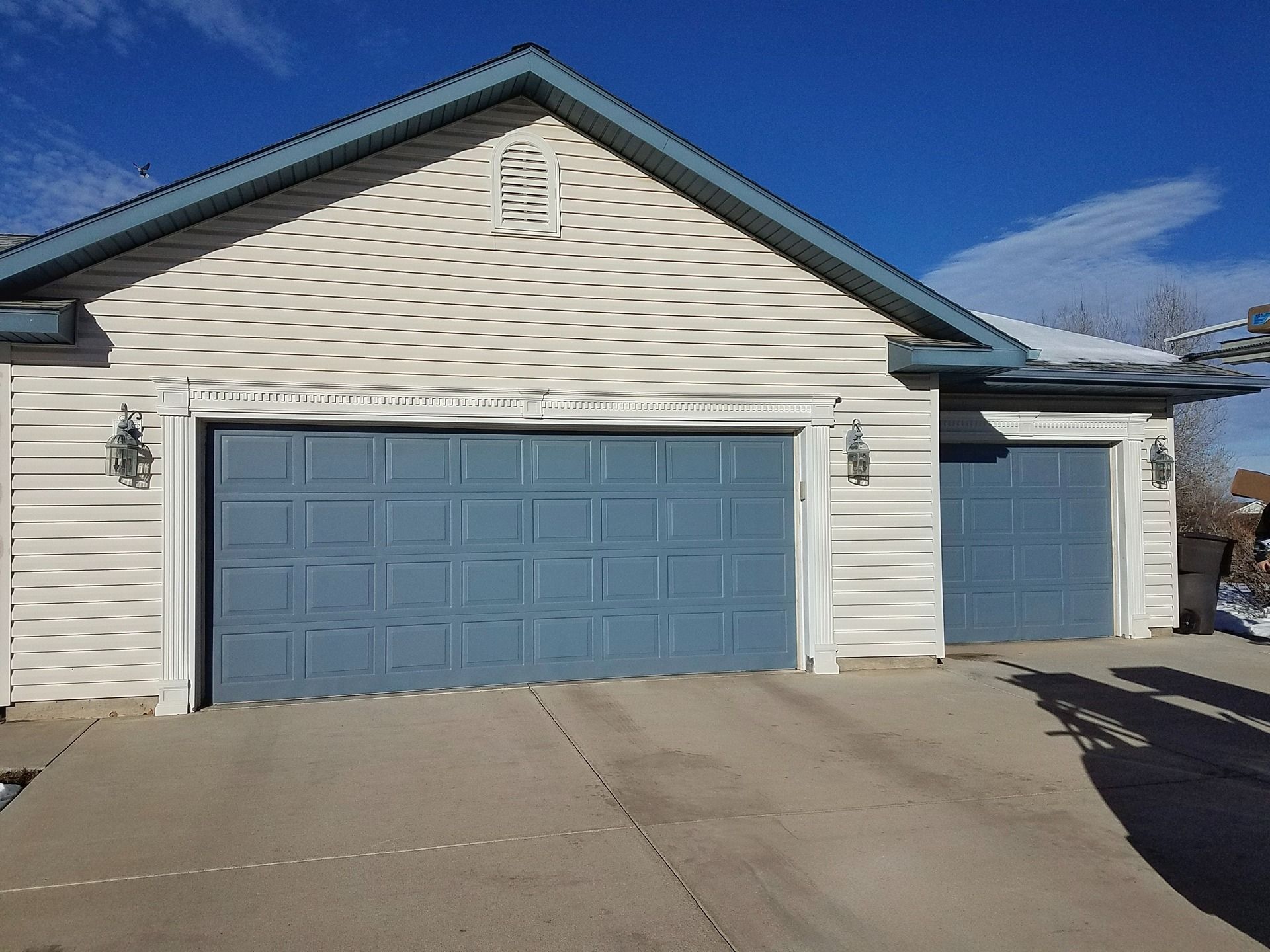 A blue two-car garage and a single-car garage with light-colored siding under a blue sky on a sunny day.