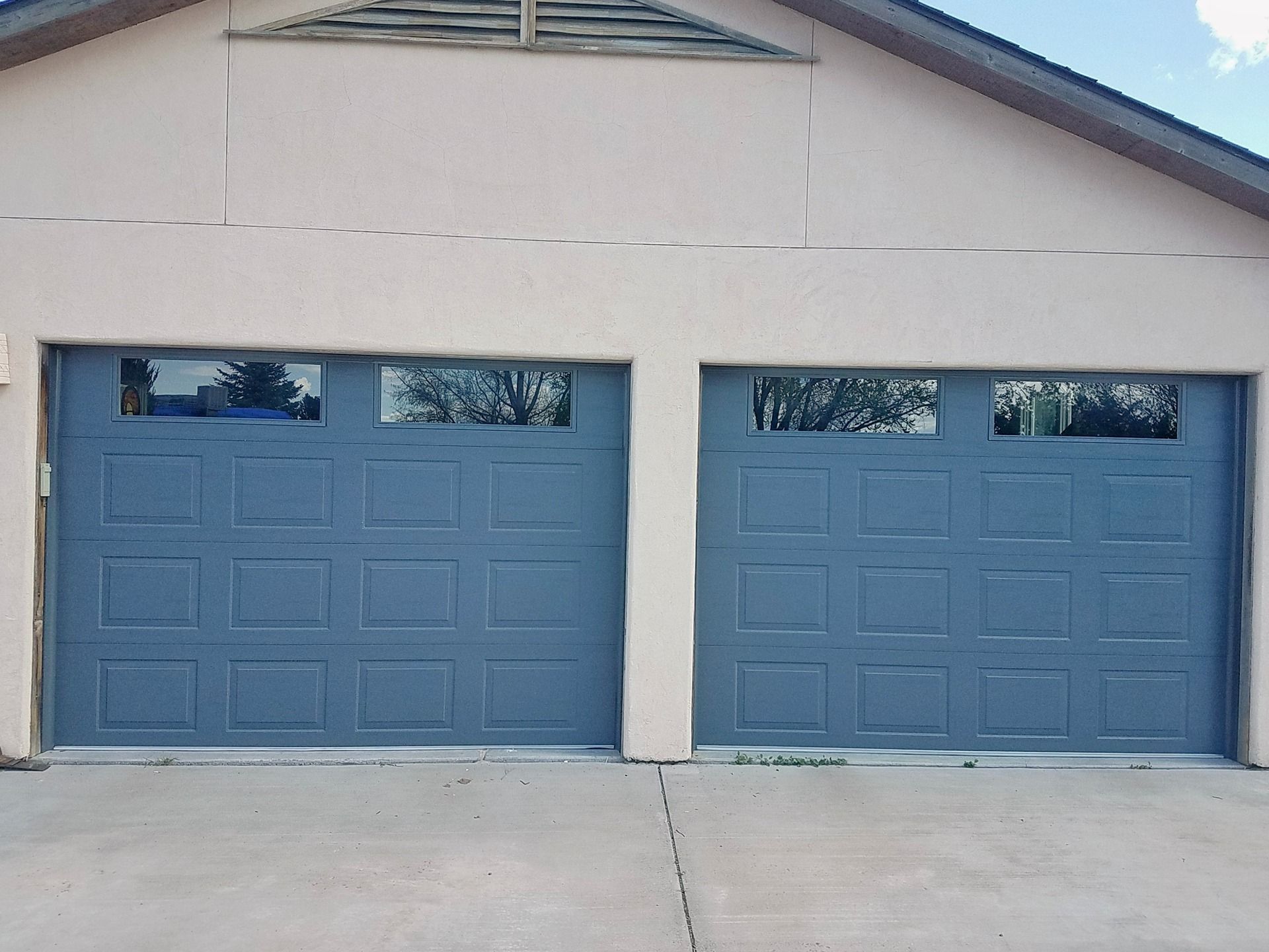 Two blue, paneled garage doors with rectangular windows, set into a beige stucco exterior.