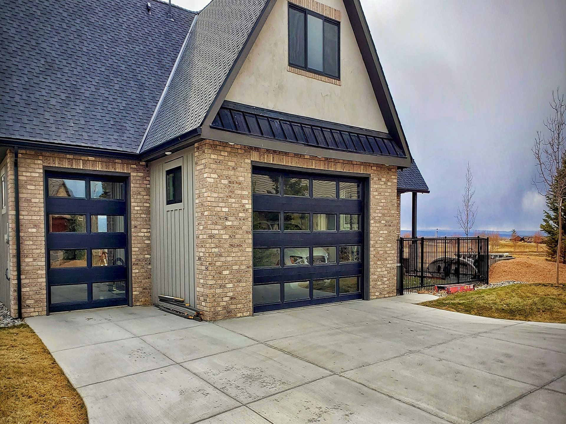A house exterior featuring a brick facade, dark metal roof, and two modern garage doors with horizontal glass panels.