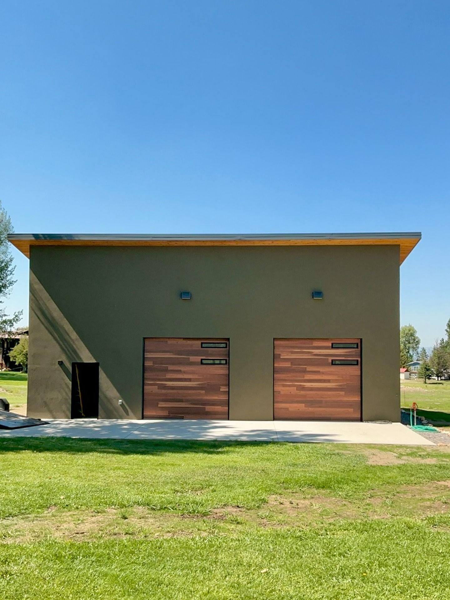 Modern building with two wood-paneled garage doors, a small side door, and exterior lights set in a grassy yard.