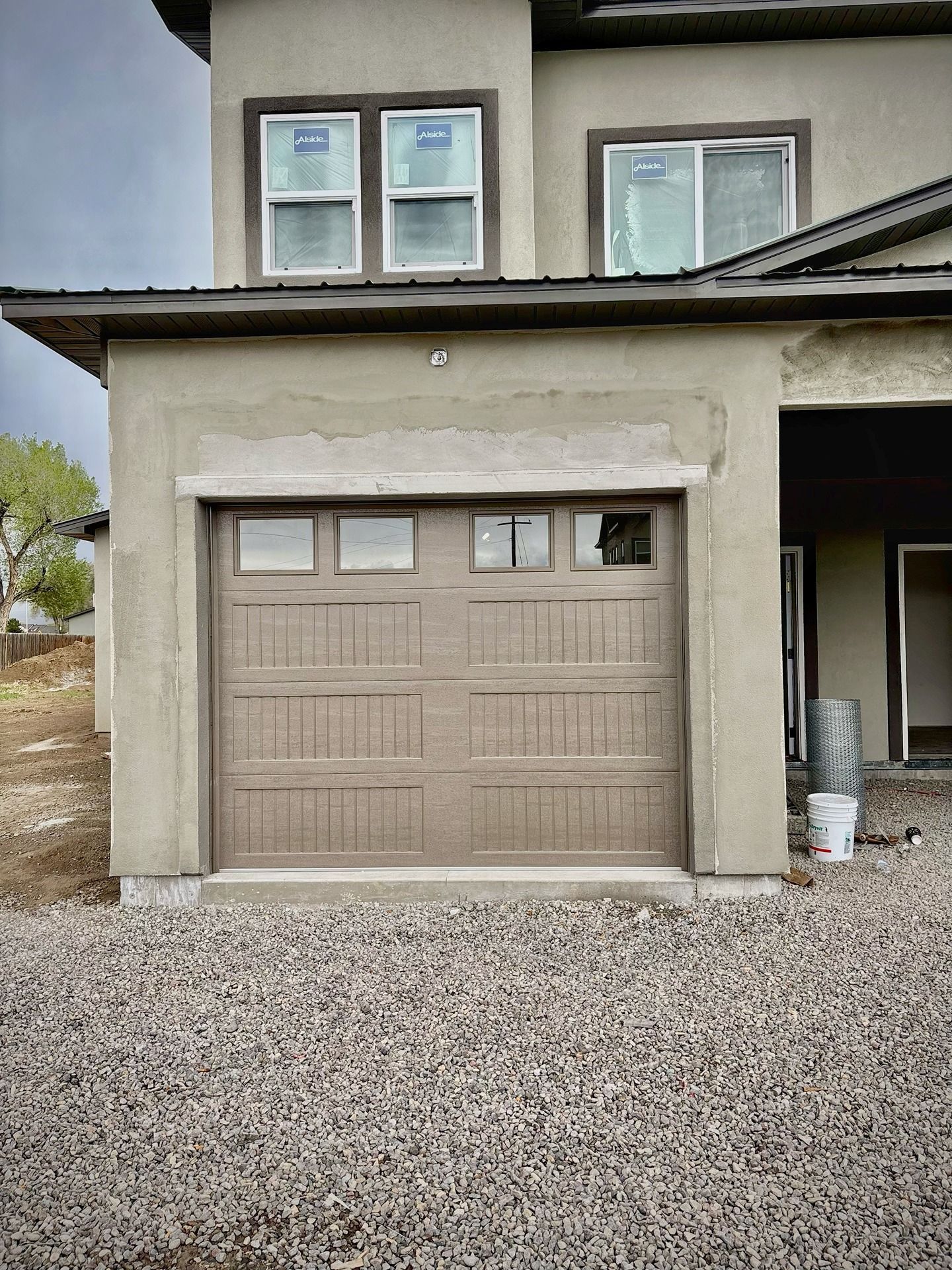 A tan, modern home exterior features a single-car garage door with windows and an unfinished stucco facade.