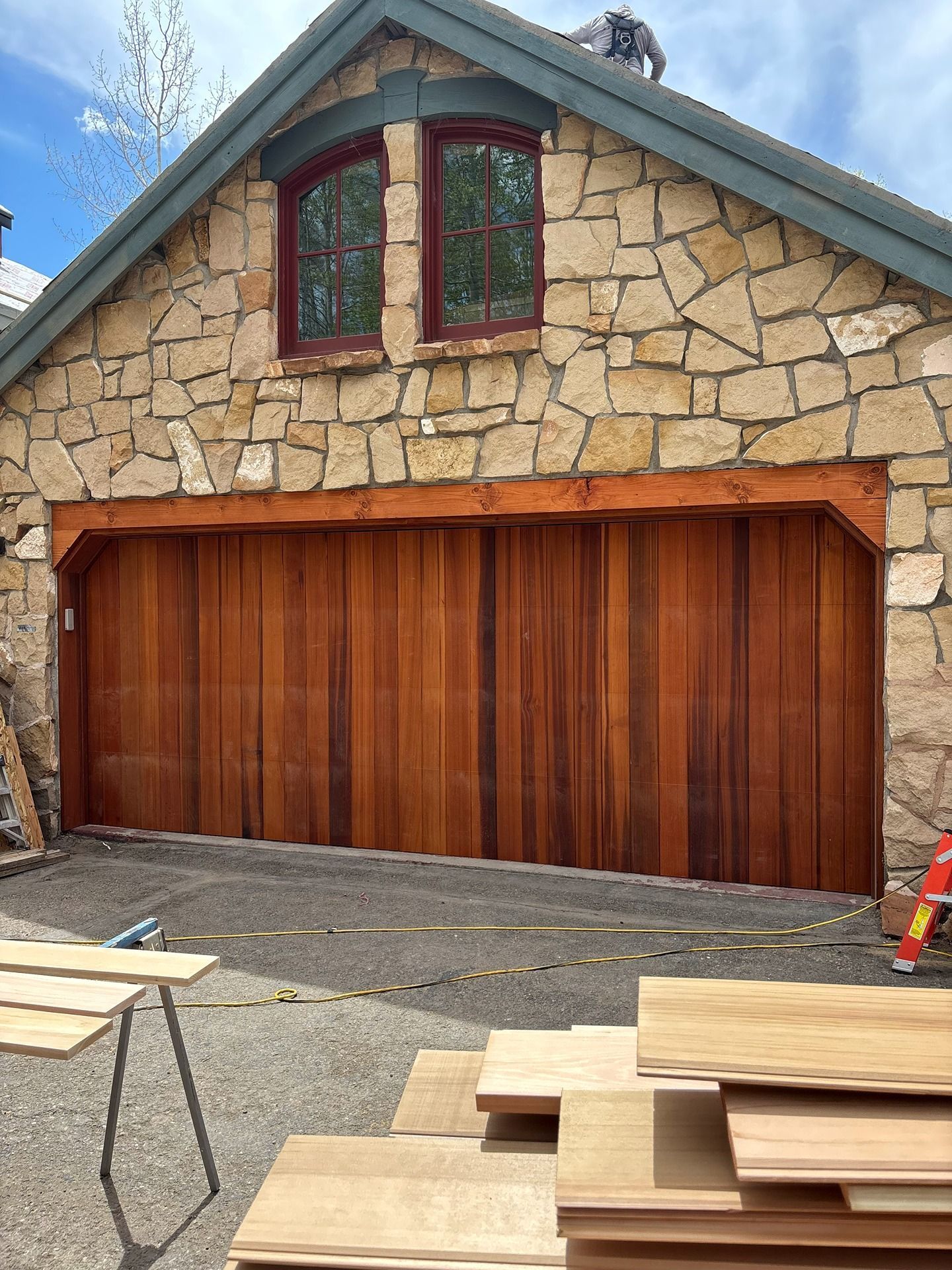 A stone garage building with a large wooden door, featuring an arched window above and construction materials in the front.