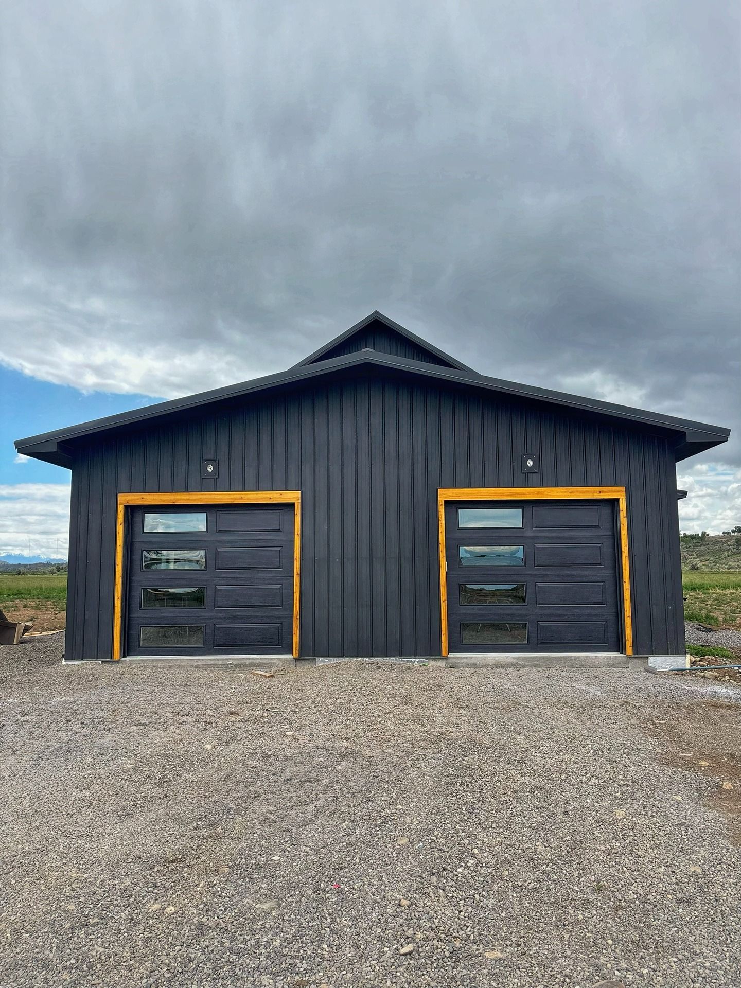 A modern black metal garage with two dark glass-paneled doors and natural wood trim, set against a cloudy sky.