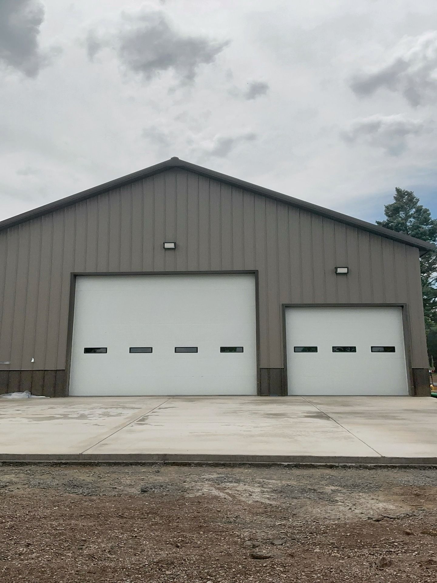 A metal-sided building with two white garage doors, each featuring a horizontal row of rectangular windows.