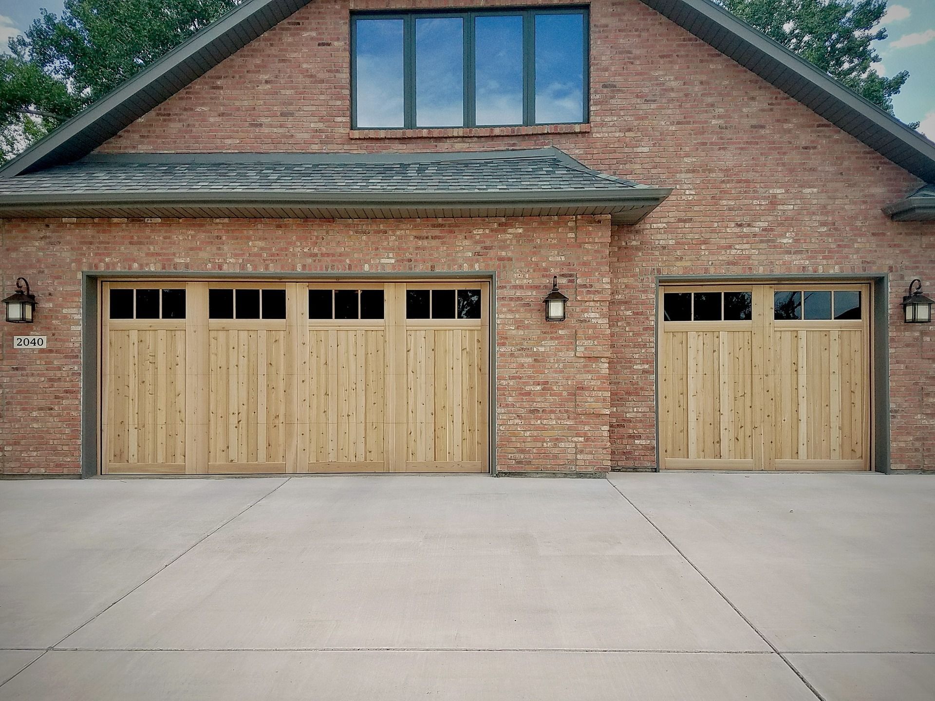 A brick building with a three-car garage and a single-car garage featuring natural wood doors and glass panels.