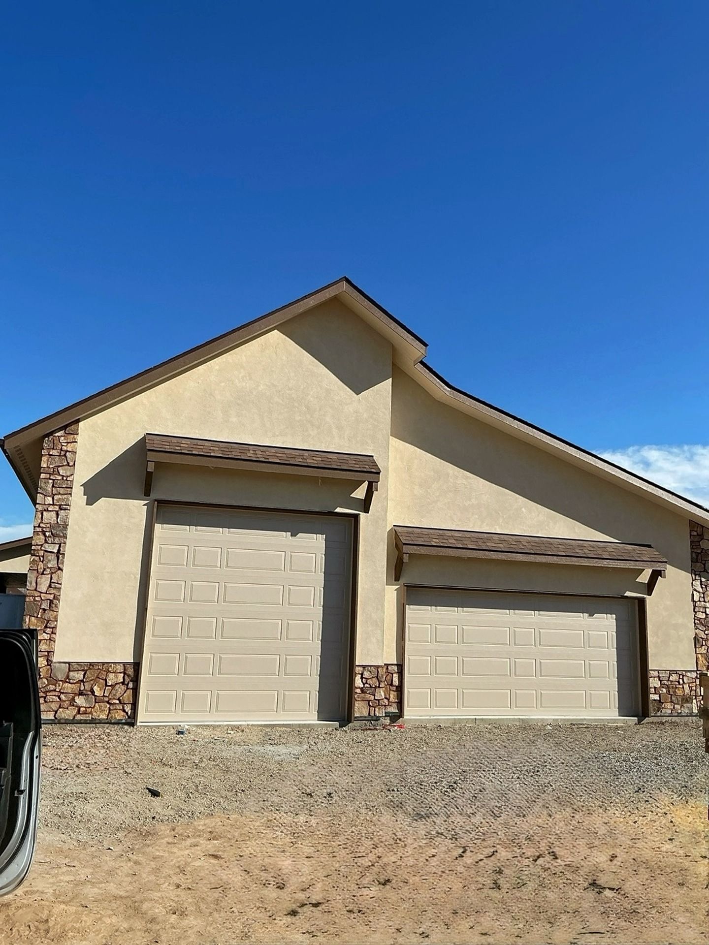 A beige, single-story house with two garage doors and stone accents on the corners under a clear blue sky.