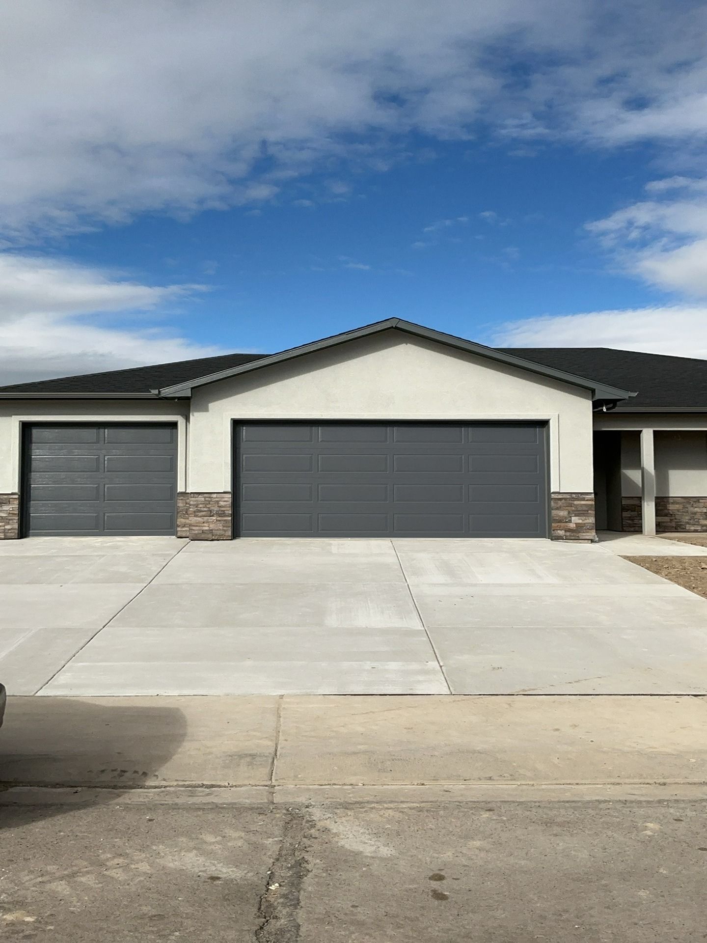 A modern house exterior featuring a two-car garage and a one-car garage with grey doors, light stucco, and stone accents.