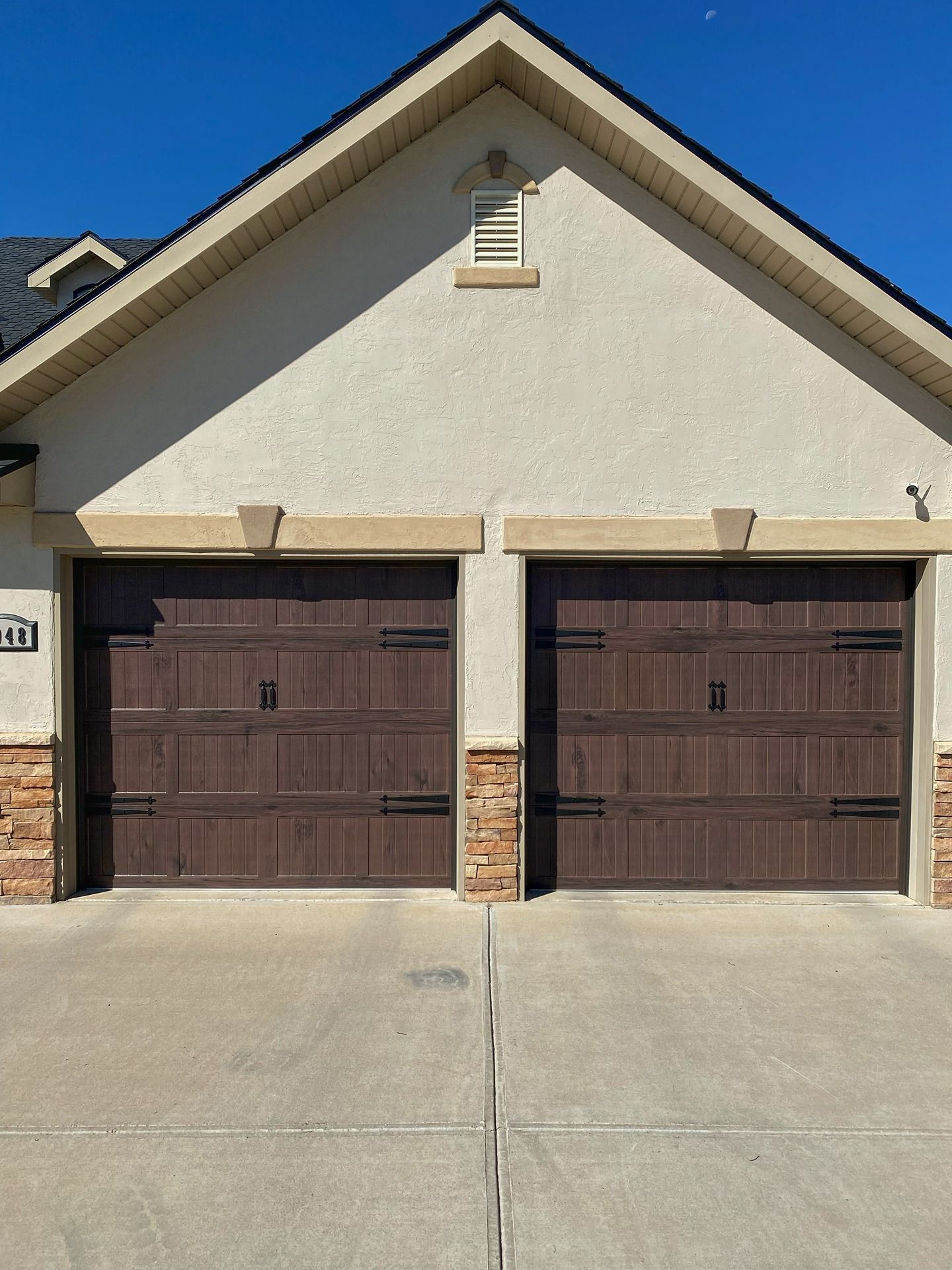 A suburban home featuring two brown, wood-paneled garage doors with black decorative hinges on a concrete driveway.