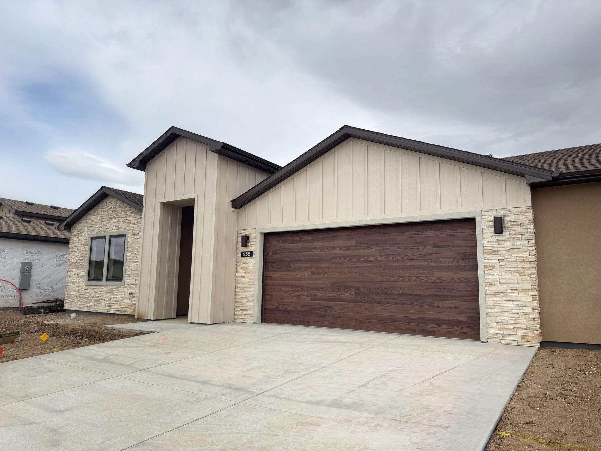 Modern beige house with dark brown garage door and wide concrete driveway under cloudy sky