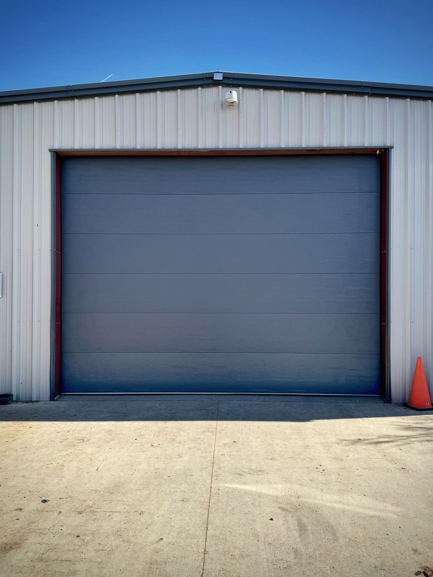 A large, blue metal garage door set into a light-colored corrugated metal building under a clear blue sky.