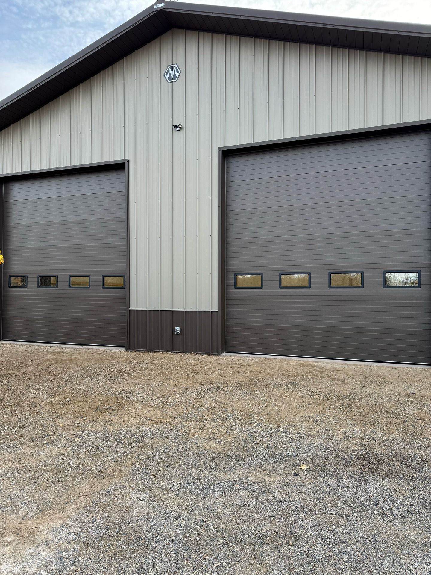 A metal building with beige siding, dark brown trim, and two matching garage doors with rectangular windows.