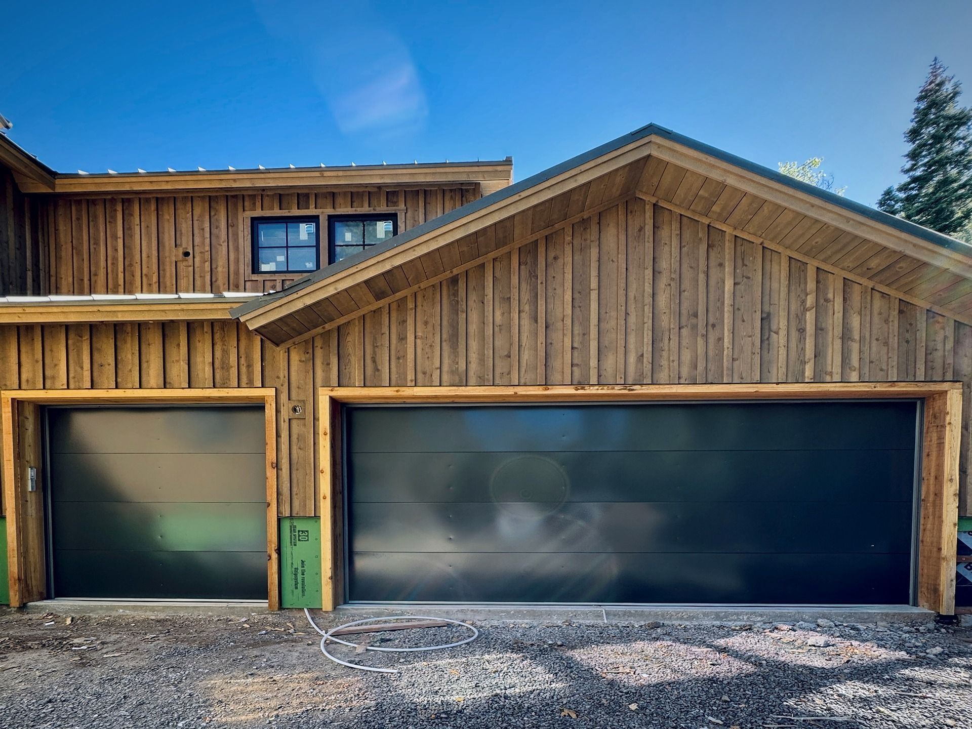 A two-car garage with modern dark gray horizontal-panel doors set into a building with rustic vertical wood siding.