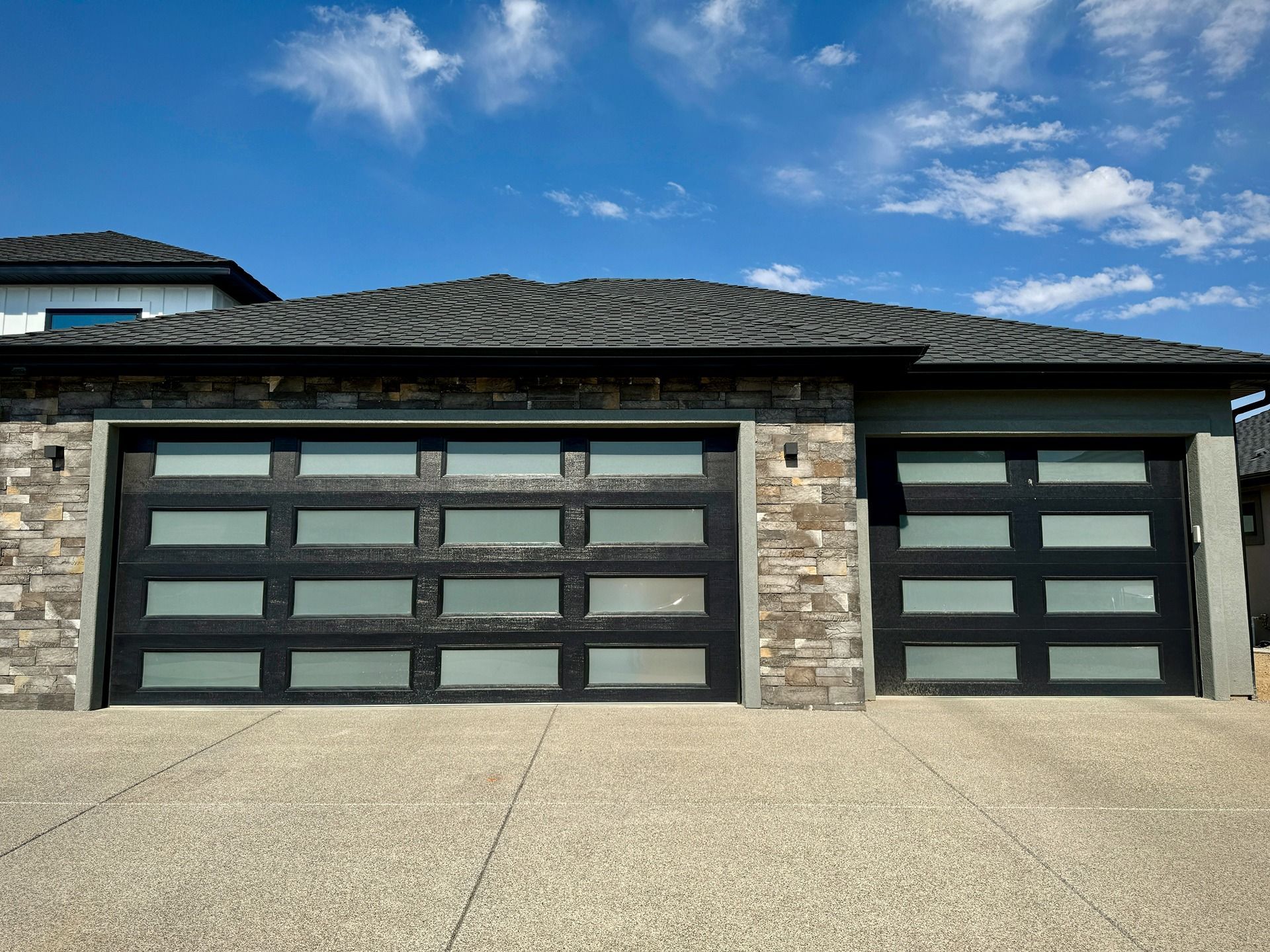 A modern house exterior featuring a two-car garage with black-framed, frosted-glass doors against a stone facade.