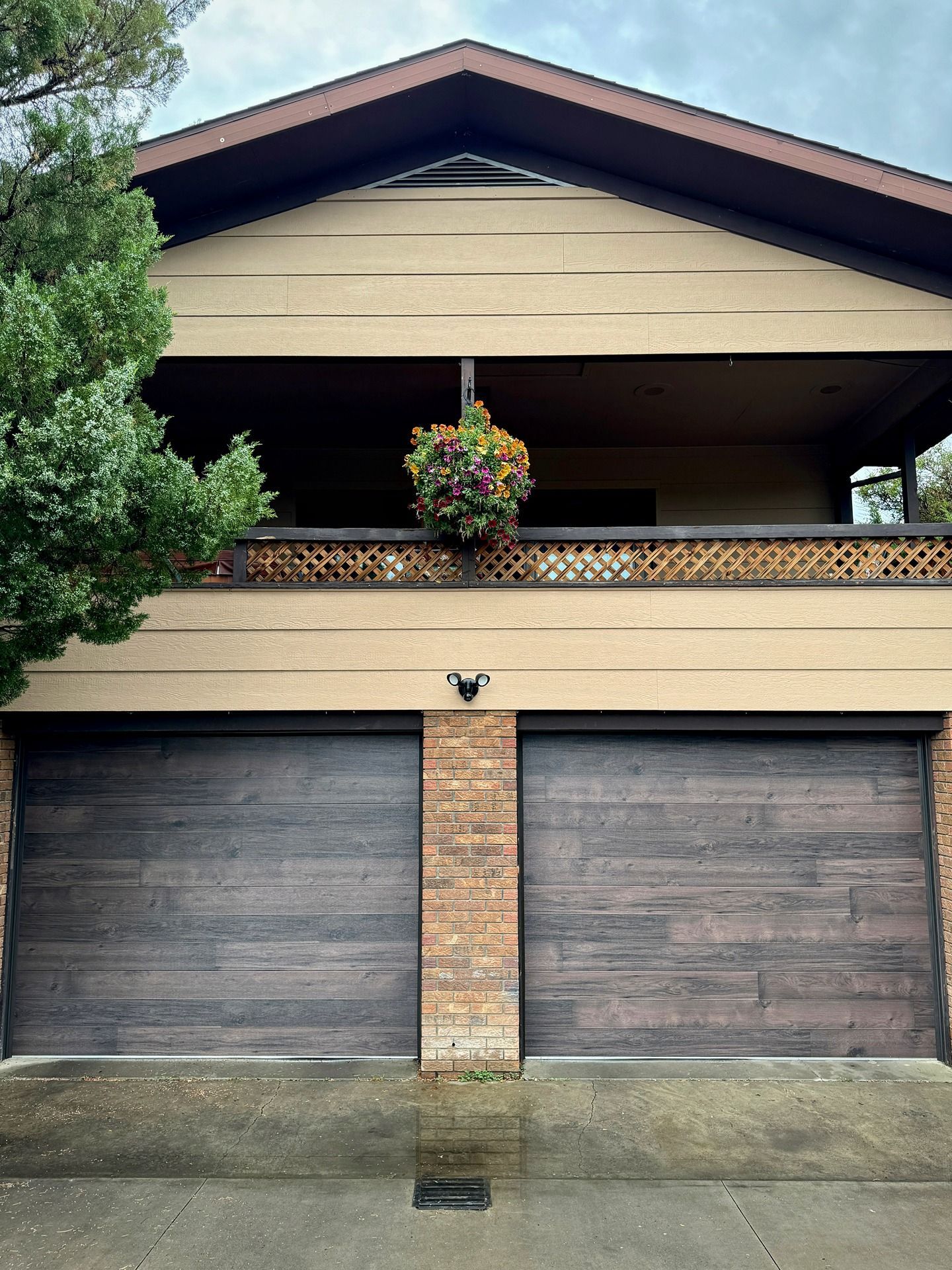 A two-story building with two dark wood garage doors and a balcony featuring a hanging flower basket.