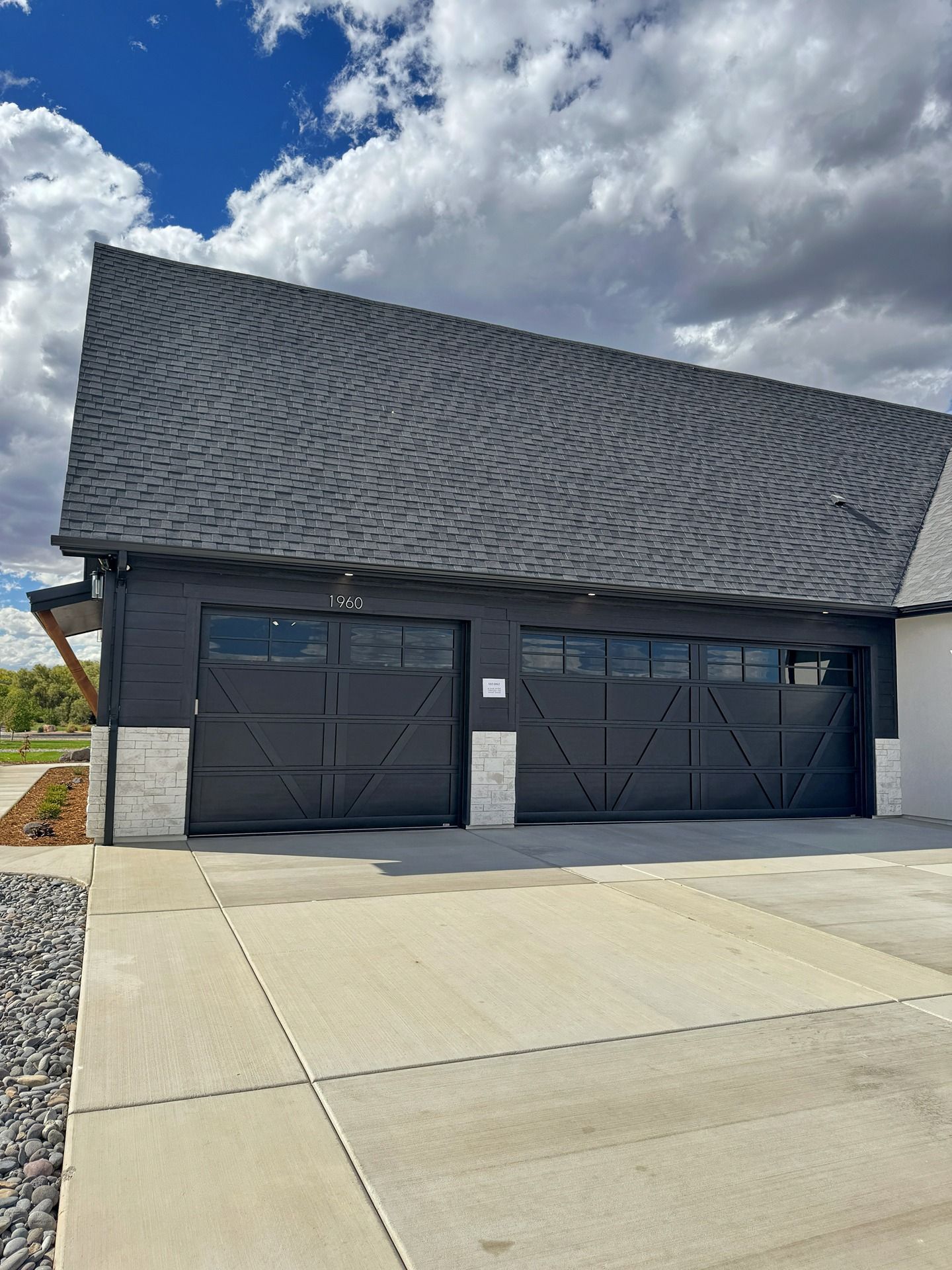 A modern garage with black, geometric-patterned doors, black siding, and light stone accents under a textured roof.