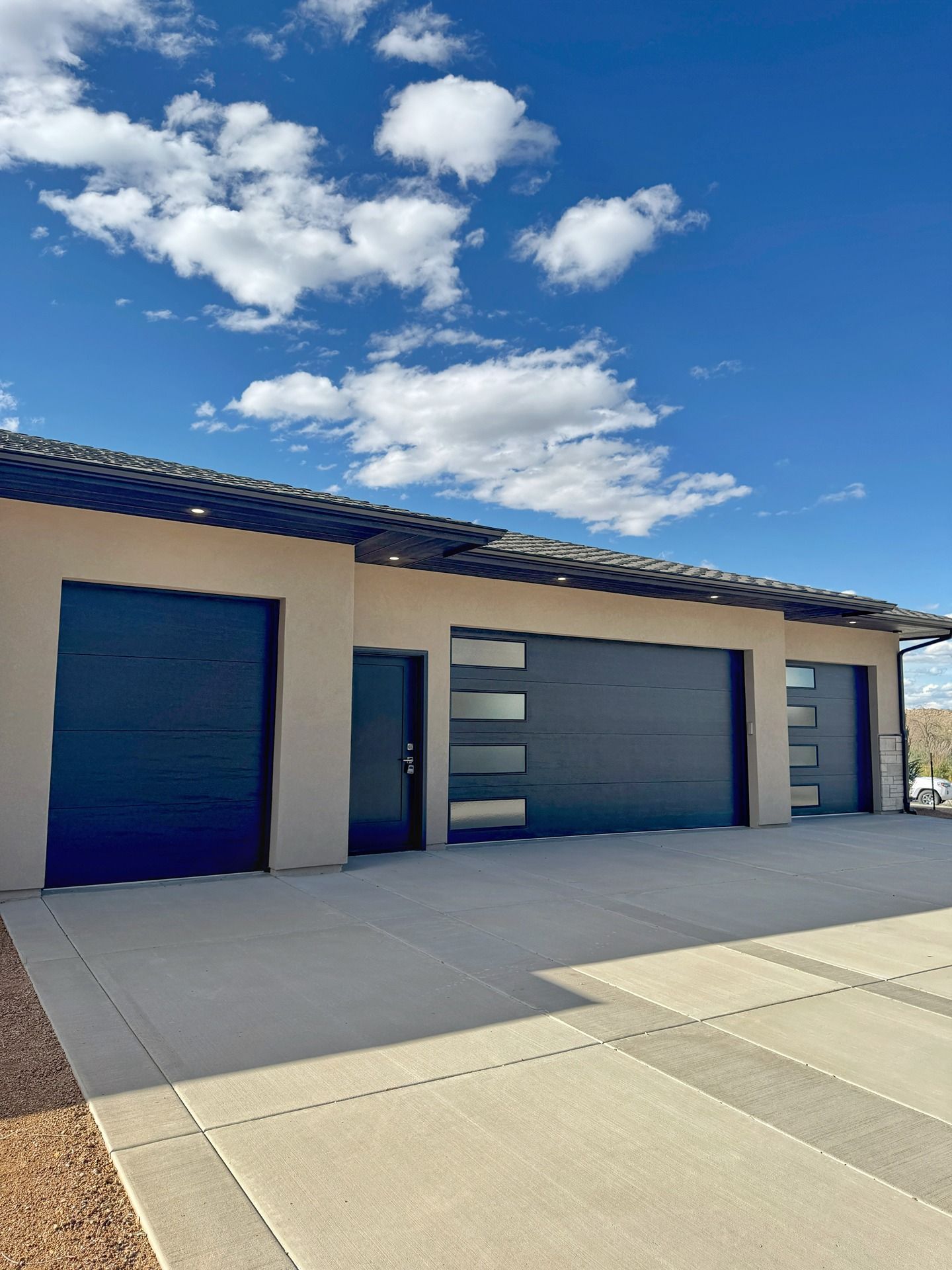 A tan building with a dark roof featuring a side door, a single garage door, and a wider double garage door with windows.