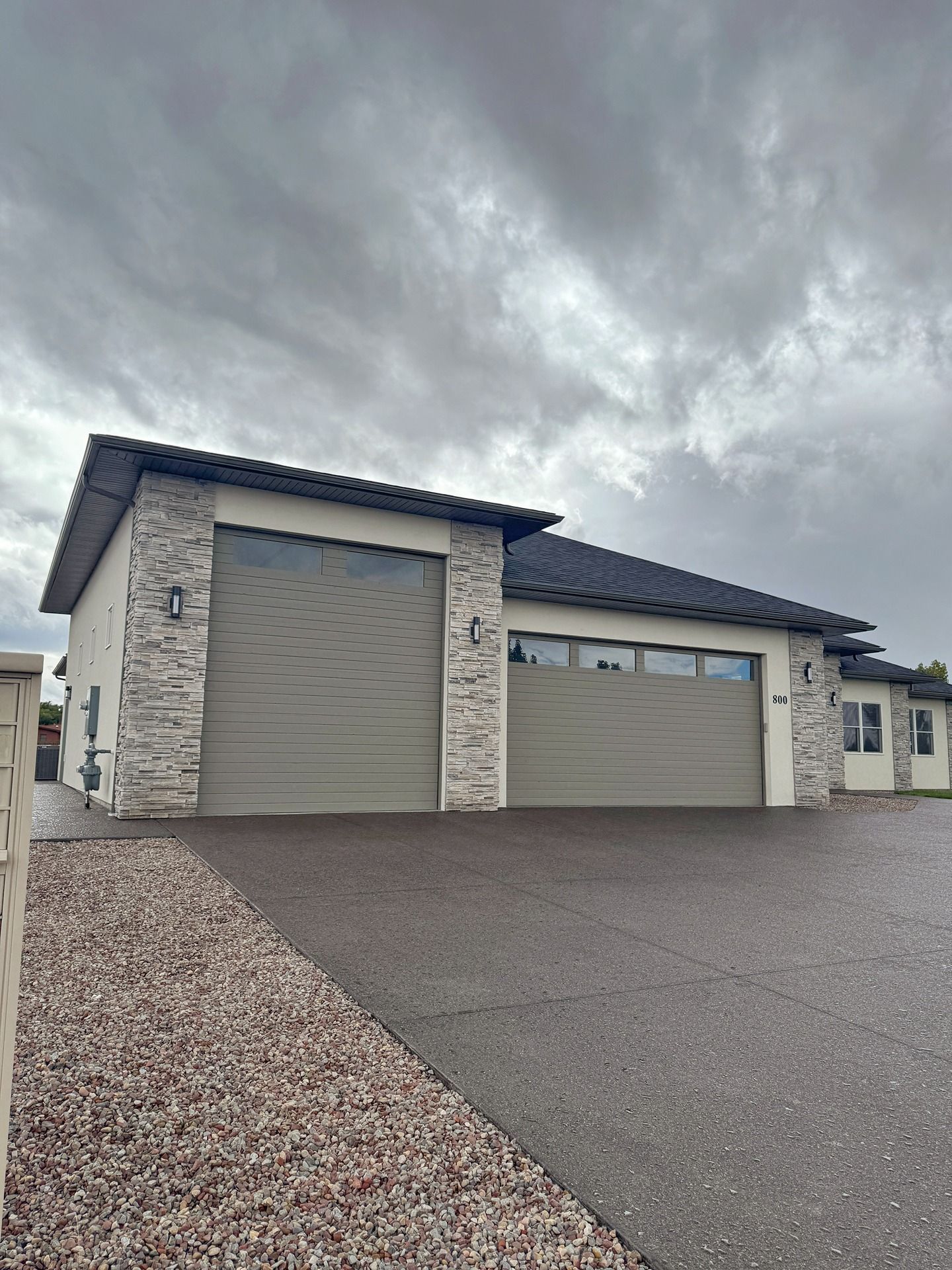 A tan house with stone corner accents and two garage doors sits under a cloudy, overcast sky.