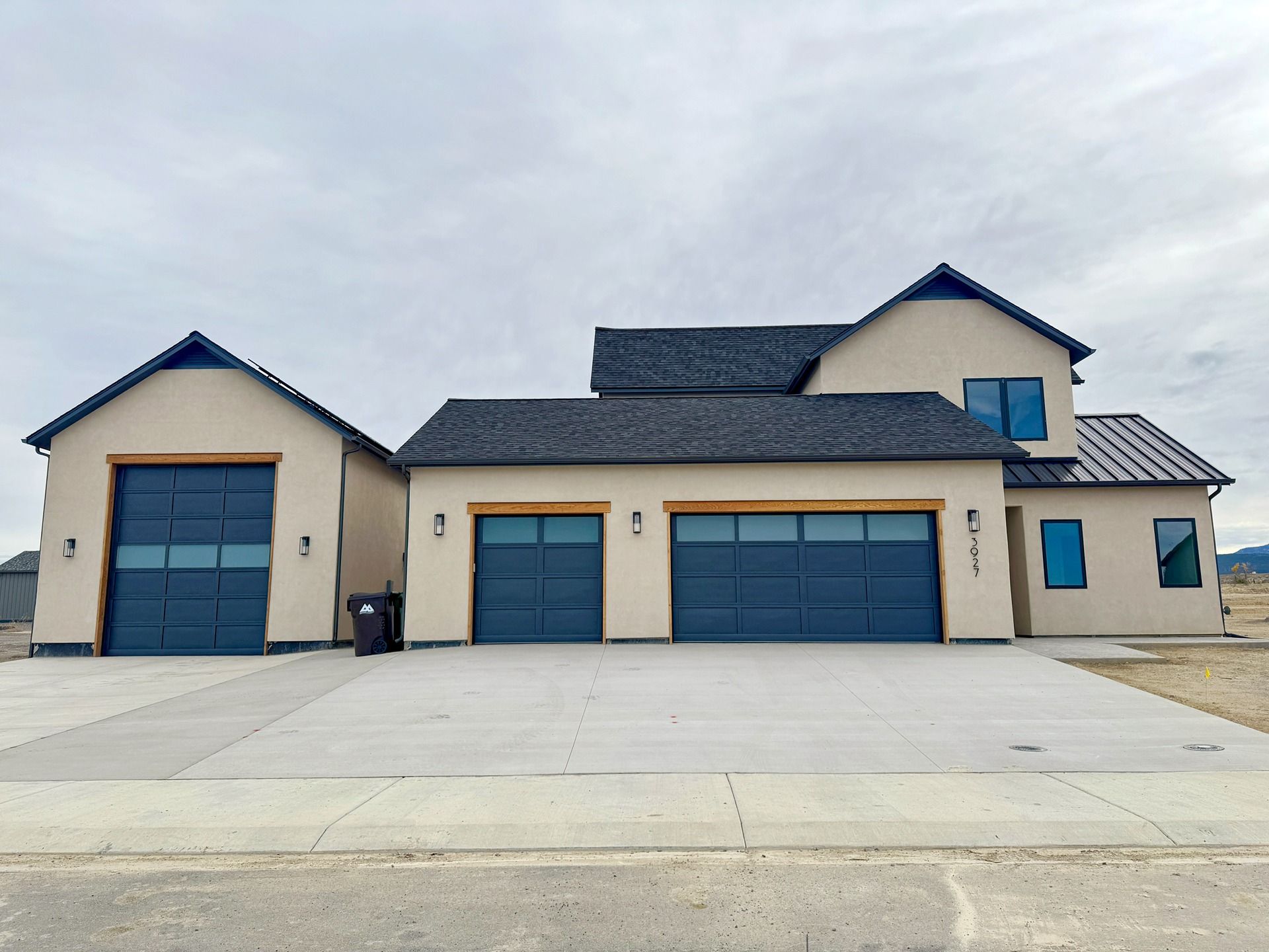 A beige two-story suburban house with a detached single-car garage, an attached two-car garage, and dark blue doors.
