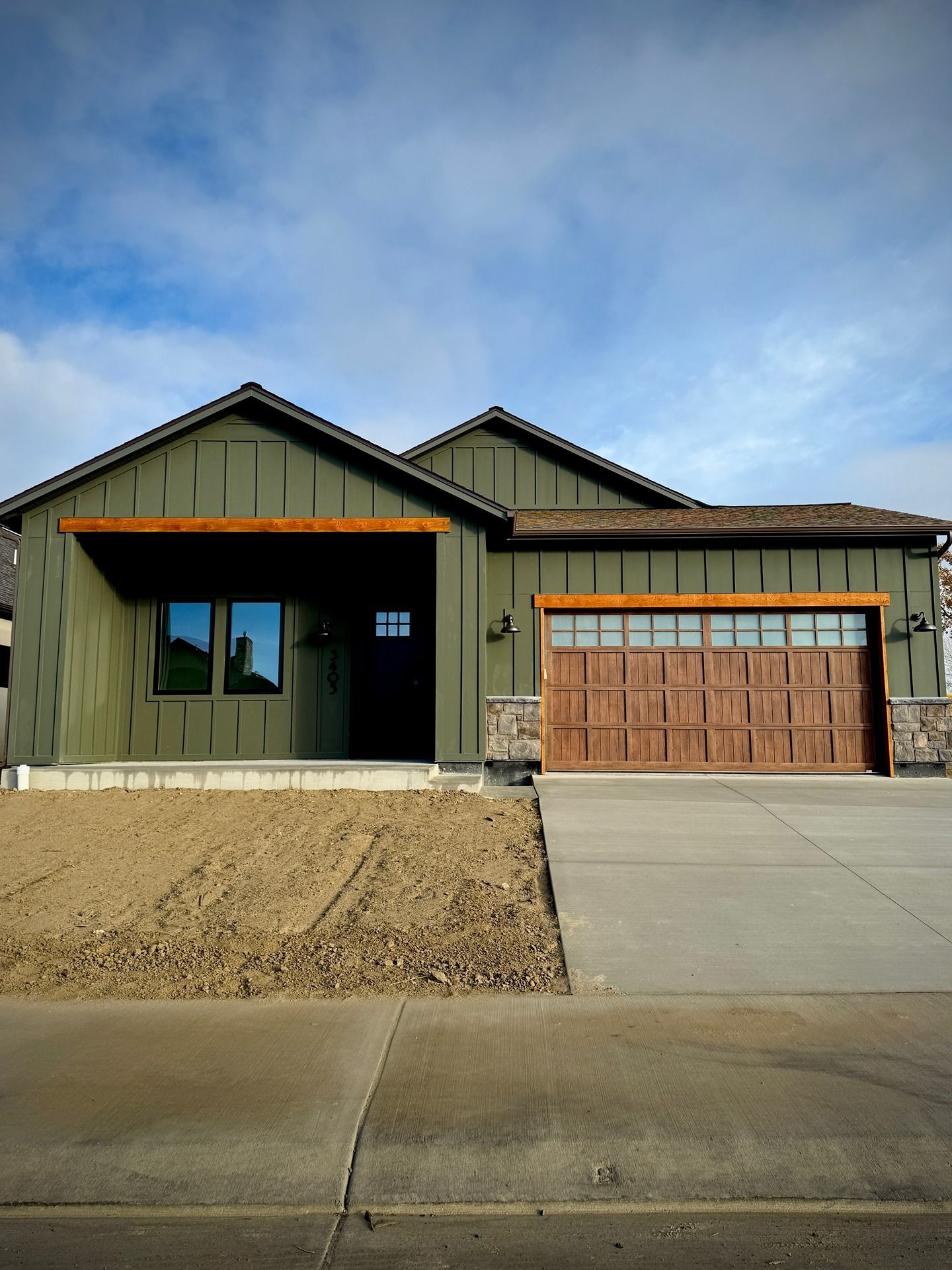 A modern single-story house with green vertical siding, a wooden garage door, and a brown wood-beam porch entry.