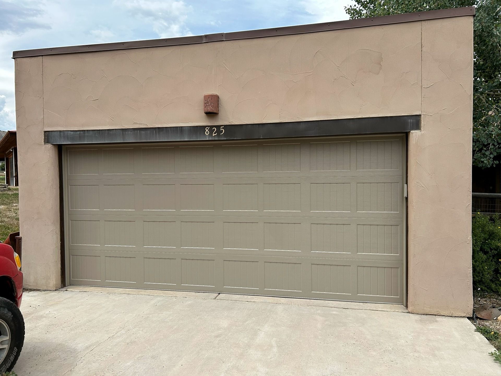 A tan stucco garage with a single beige paneled door and the number 825 centered above the opening.