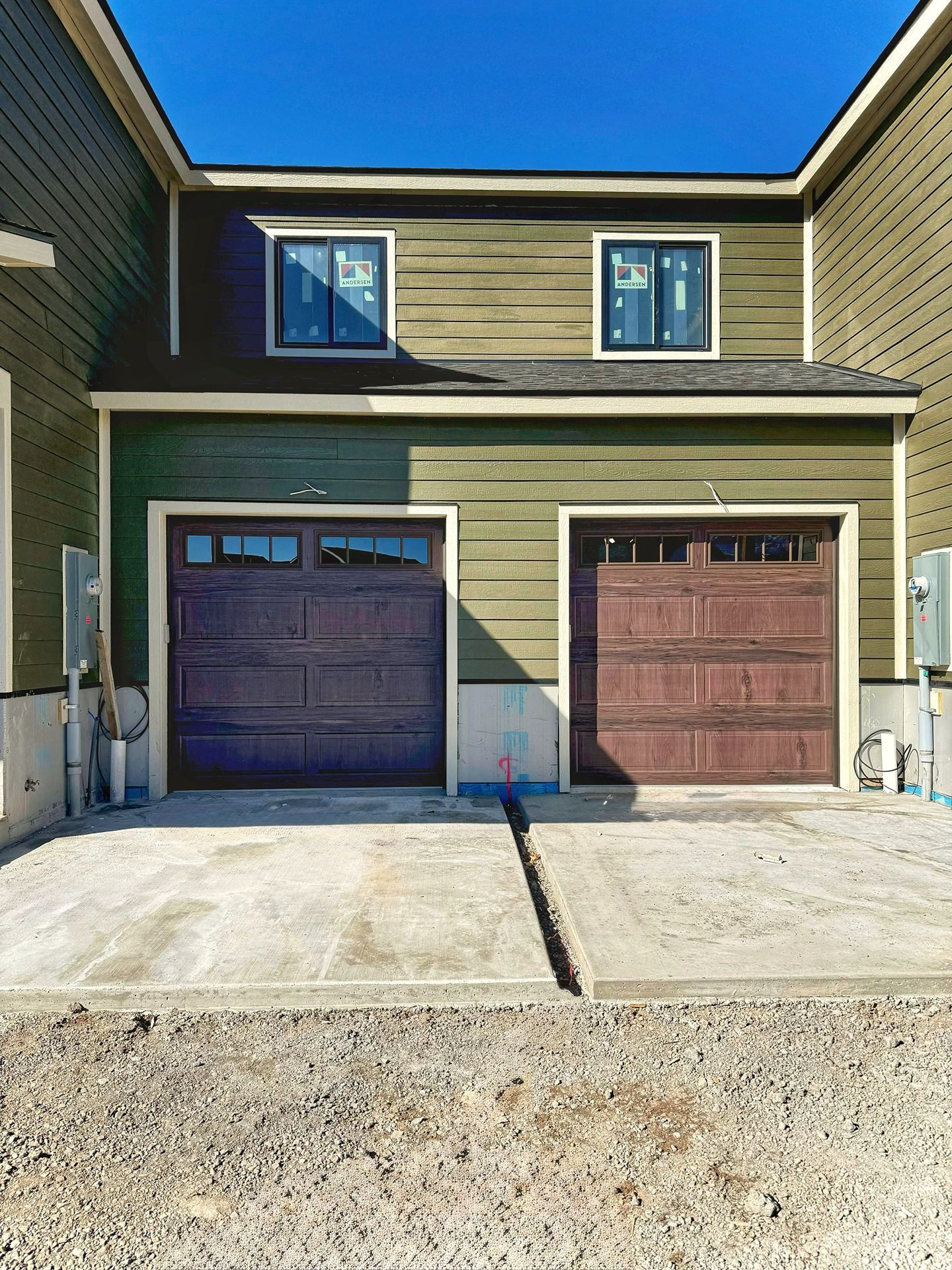A green two-story townhome exterior with two dark wood garage doors, two upper windows, and a concrete driveway.