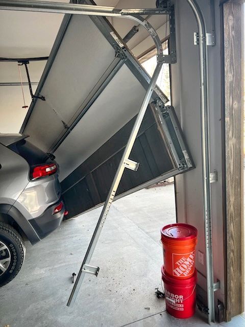 Car half-stuck under a bent garage door next to a red fire extinguisher.